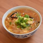 Hot and Sour Soup in a Chinese Patterned soup bowl with green onion garnish on a wooden table