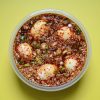 5 boiled eggs in a soy based marinade, in a circular container on yellow background.