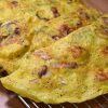 three Vietnamese yellow crispy pancakes laying on a rack. Close up shot.