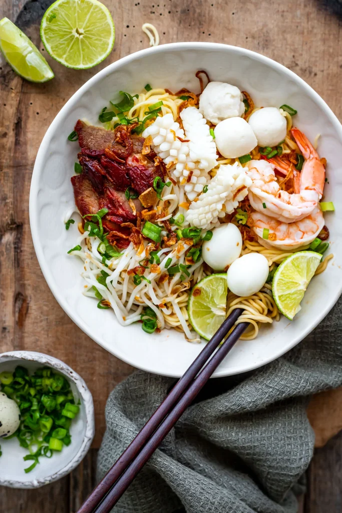 Best Vietnamese Soups: Hu Tieu but in a dry form, birds eye view of what a bowl of hu tieu (dry) looks like. There are beansprouts, squid, prawns, fish balls, pork, lime and chopsticks.