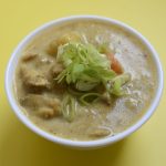 Vietnamese chicken curry (Ca Ri Ga) in a small bowl with spring onion as garnish on yellow background